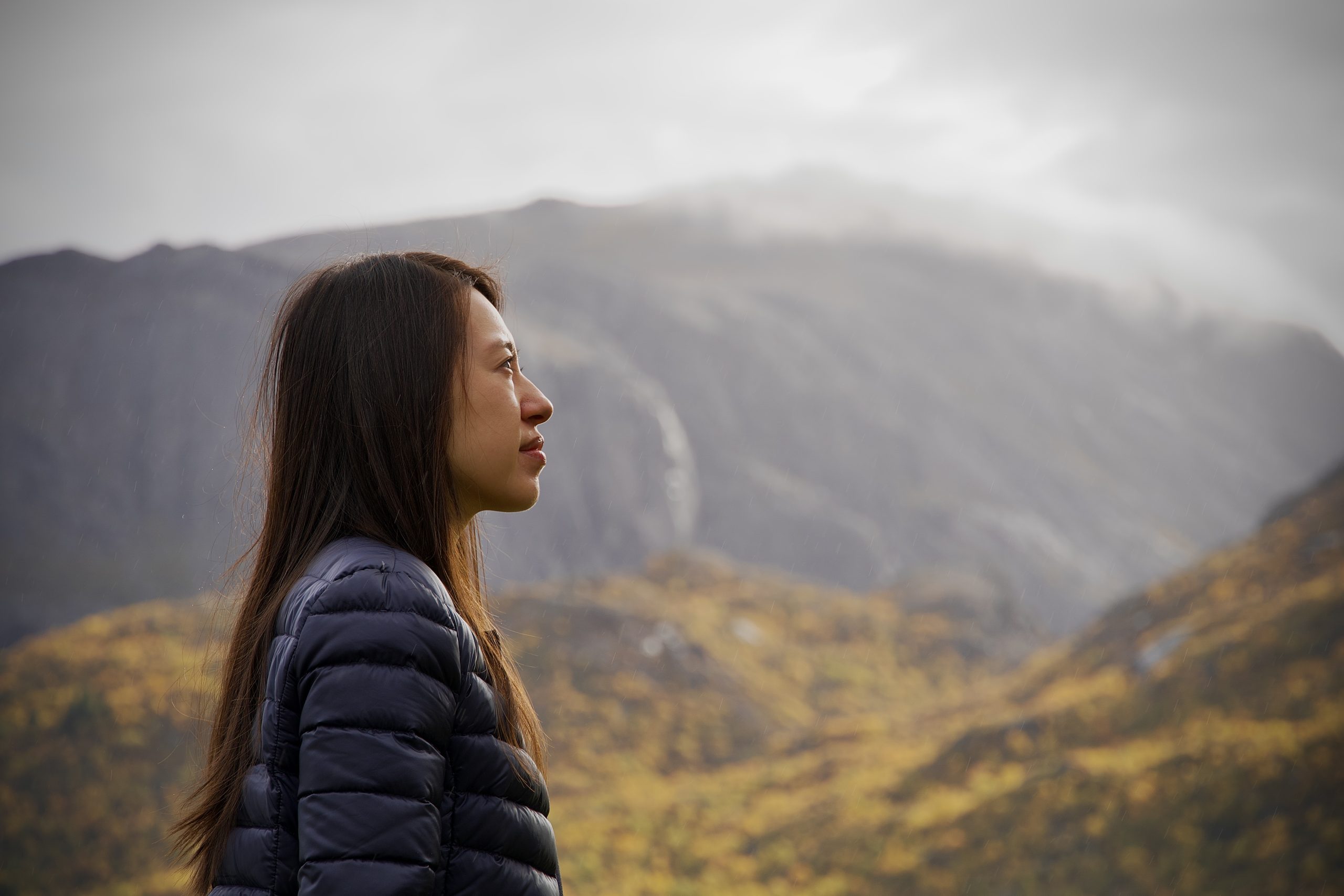 Woman in a dark jacket looking toward misty mountains.