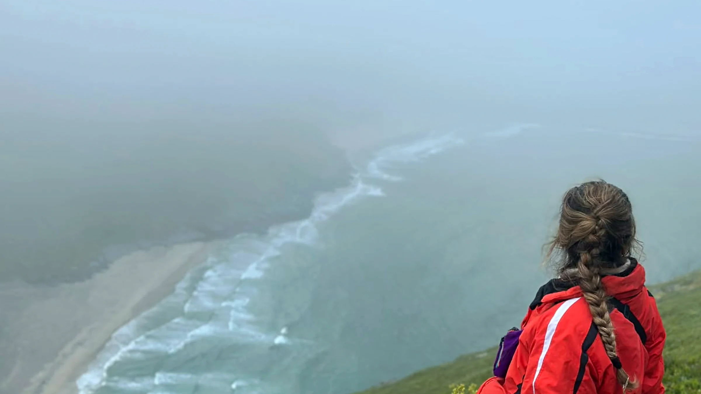 Guest in a red jacket overlooking misty Kvalvika Beach from Ryten